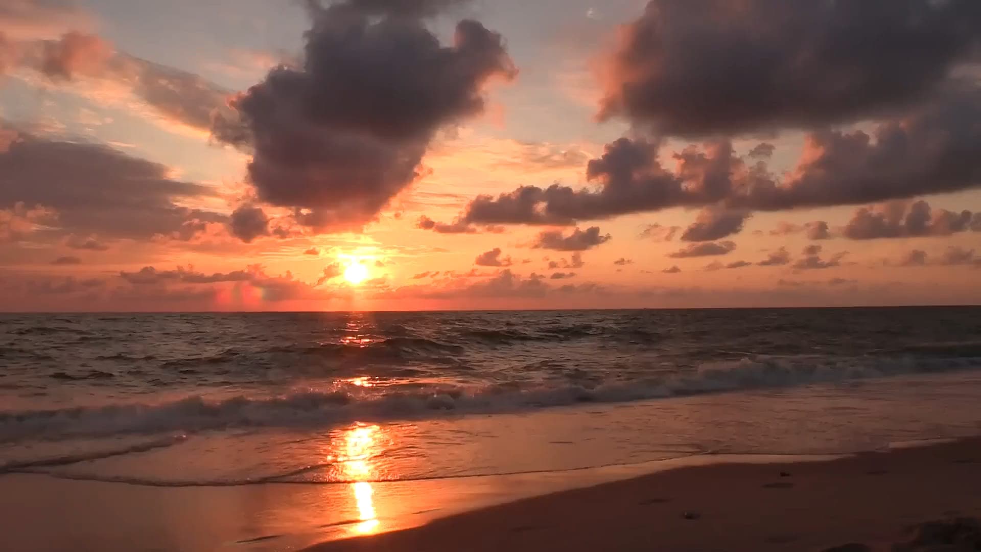 Atardecer sobre el mar, con olas llegando a la playa.